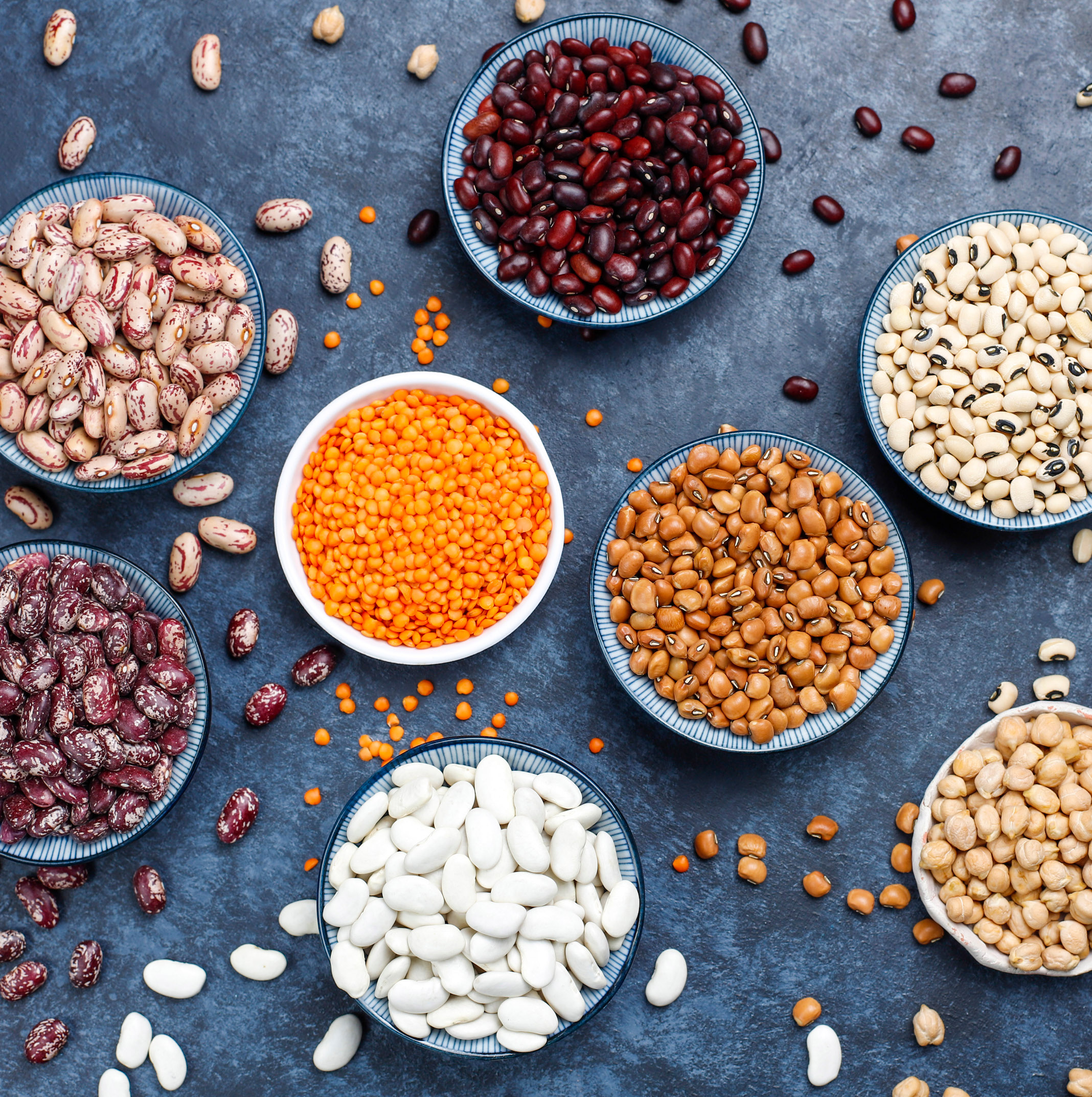 Legumes and beans assortment in different bowls on light stone b